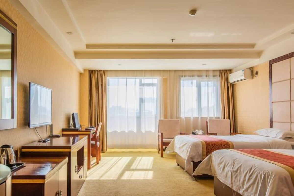 Een hotelkamer met twee bedden, een bureau, een stoel, een televisie en een groot raam met gordijnen.