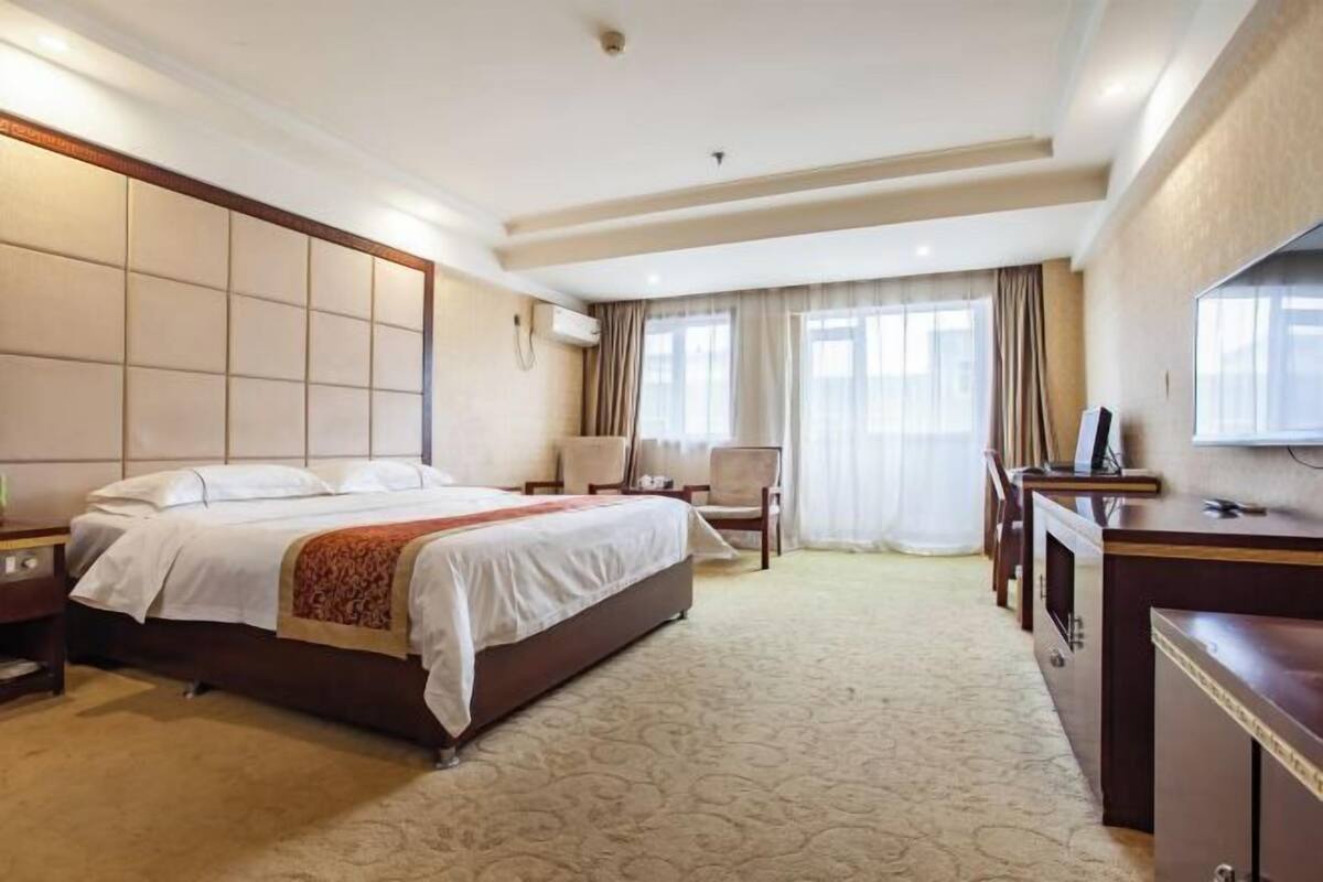 A hotel room with a large bed, a desk, a chair, and a television.