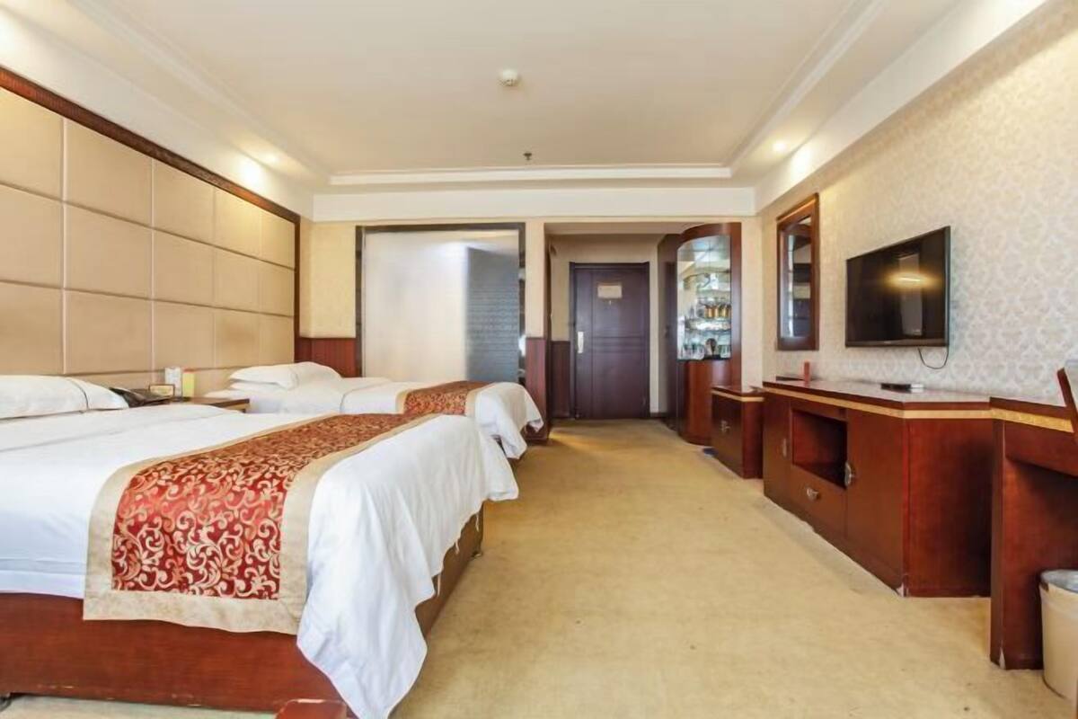 A hotel room with two beds, a TV, a desk, and a bathroom visible through an open door.