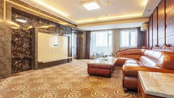 A spacious living area with a brown patterned carpet, a leather sofa, a glass coffee table, and a marble accent wall.