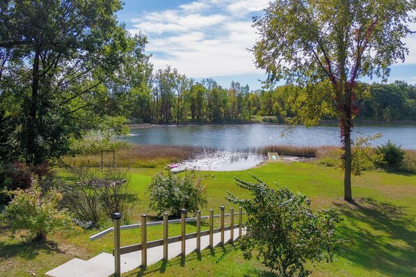 A lakeside view with a wooden deck, grassy areas, and trees.