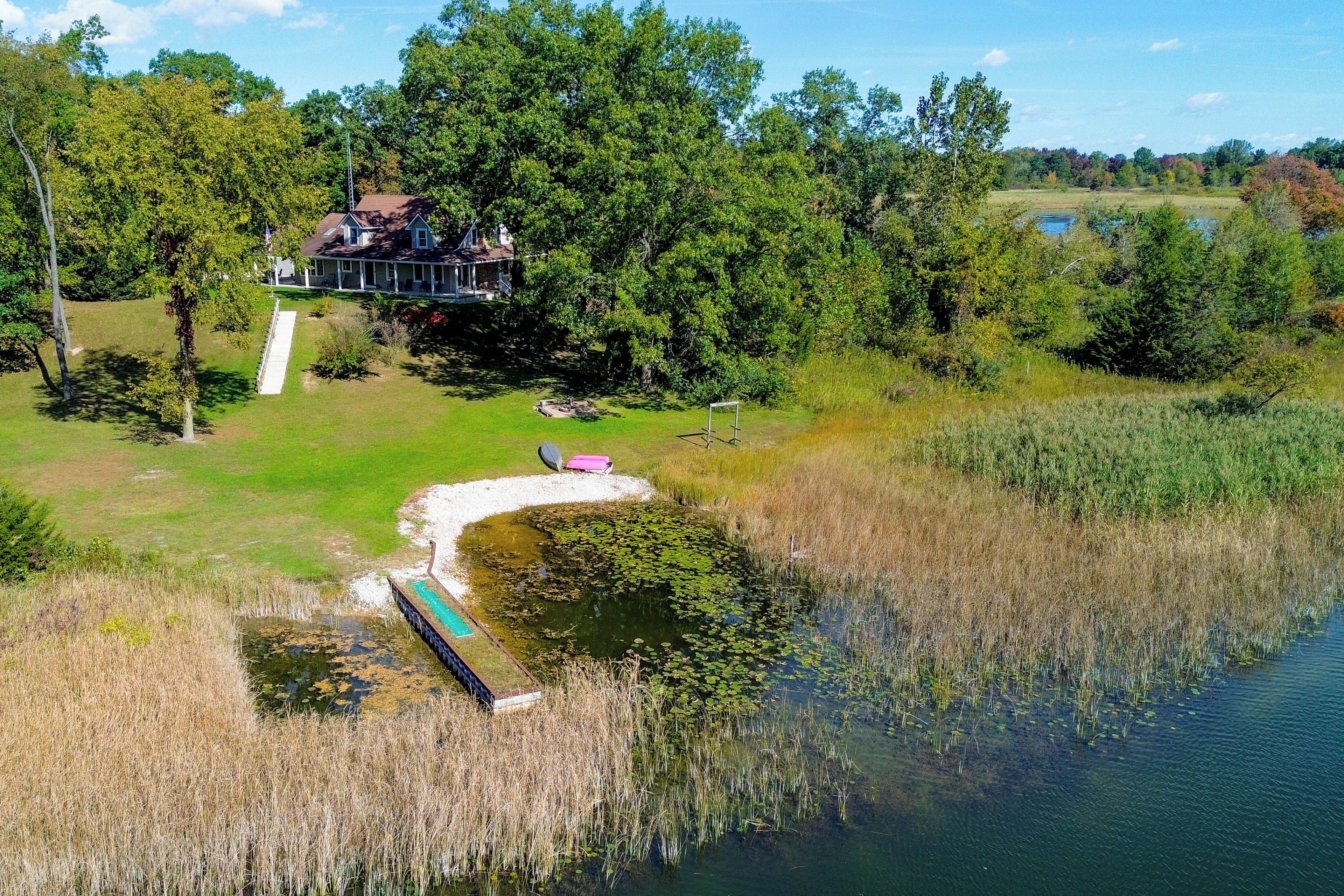 Une propriété au bord du lac, comprenant une grande maison, un quai et un étang parsemé de nénuphars.