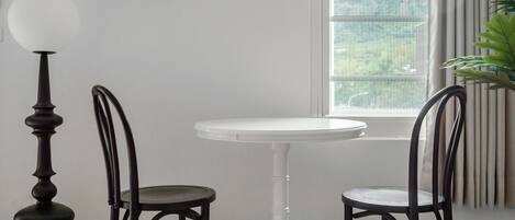 A white round table with two black chairs, a dark floor lamp, and a window with blinds.