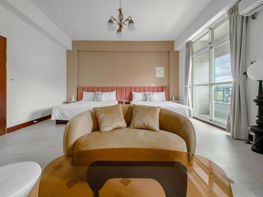 Quarto de hotel com uma cama grande, um sofá, um candelabro e vista para o exterior.