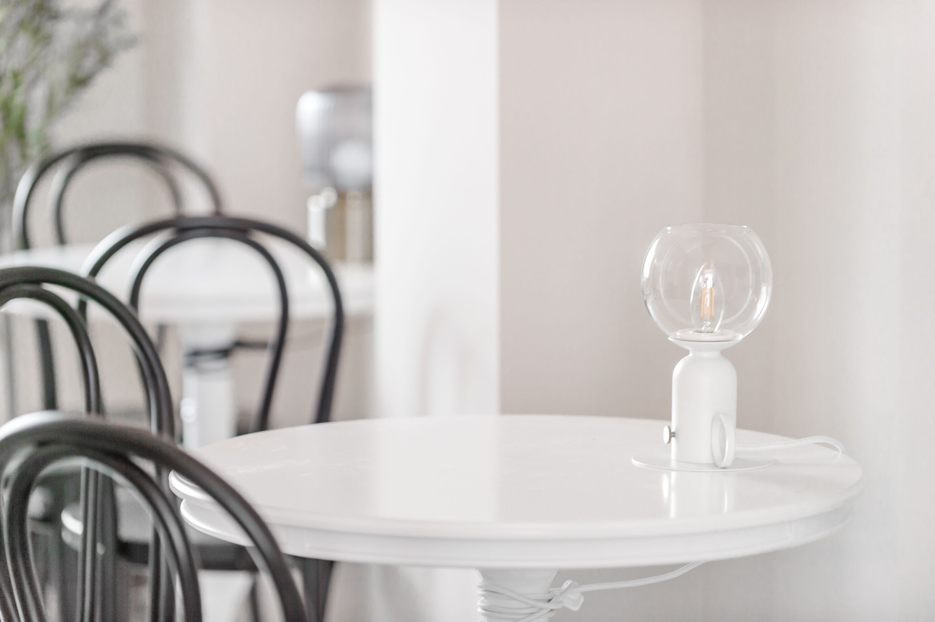 Una mesa redonda blanca con una copa de vino, rodeada de sillas negras.