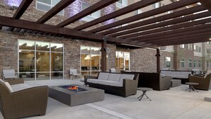 An outdoor patio area with wicker furniture, a fire pit, and a stone wall backdrop. - Holiday Inn Express & Suites Ontario - Chino Hills by IHG (Chino Hills)
