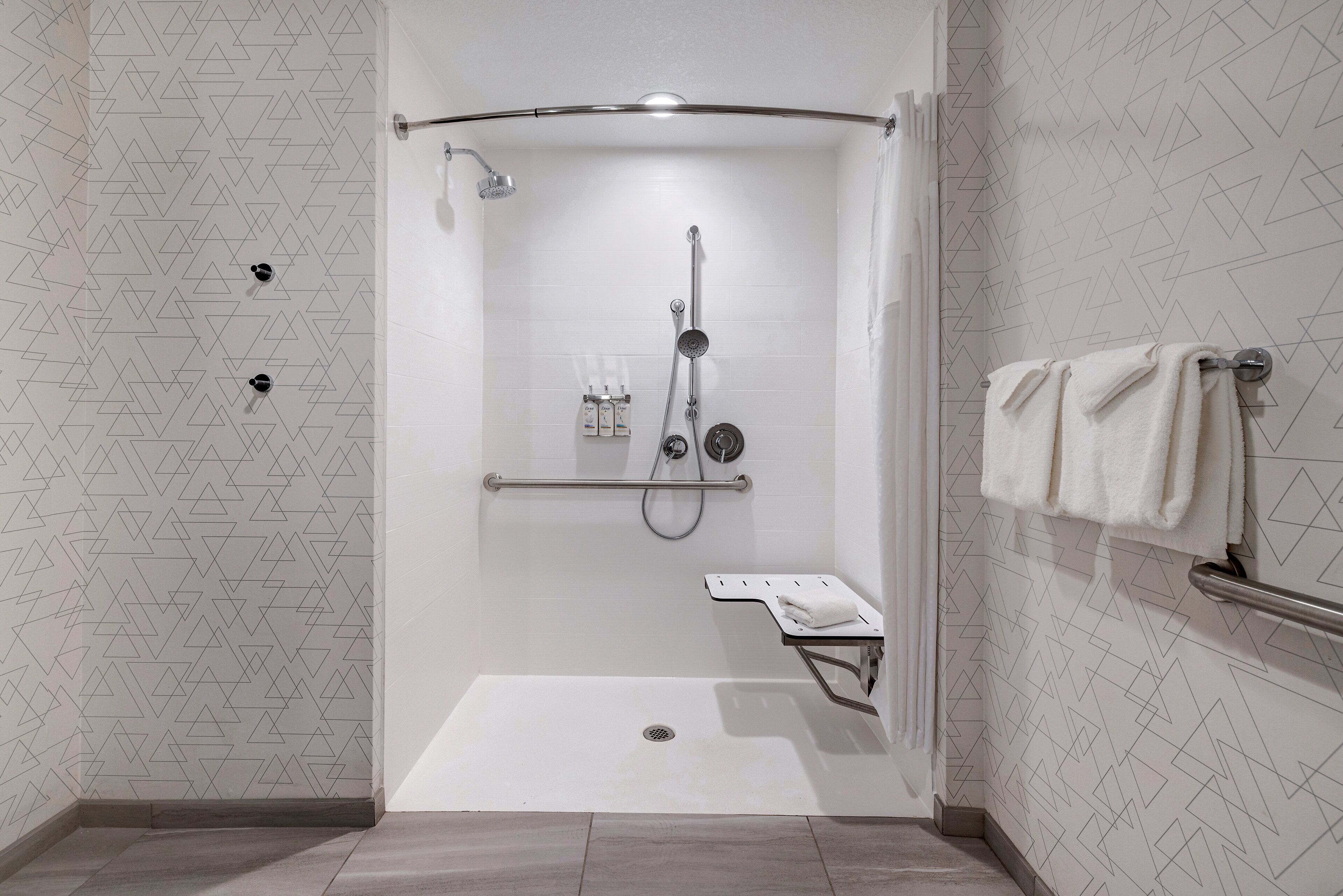 A walk-in shower with a handrail, a towel rack, and a small shelf.