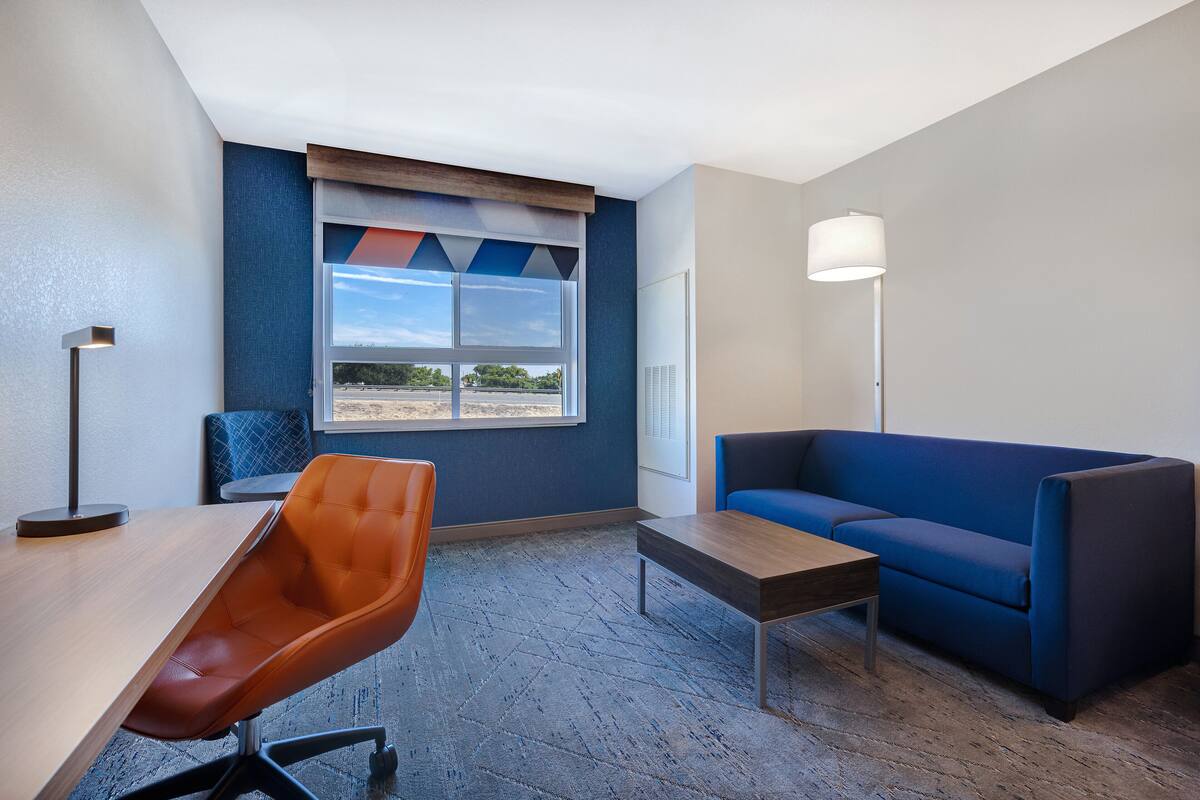 Una habitación de hotel moderna con un ventanal grande, un sofá azul, una mesa de madera y una silla marrón.