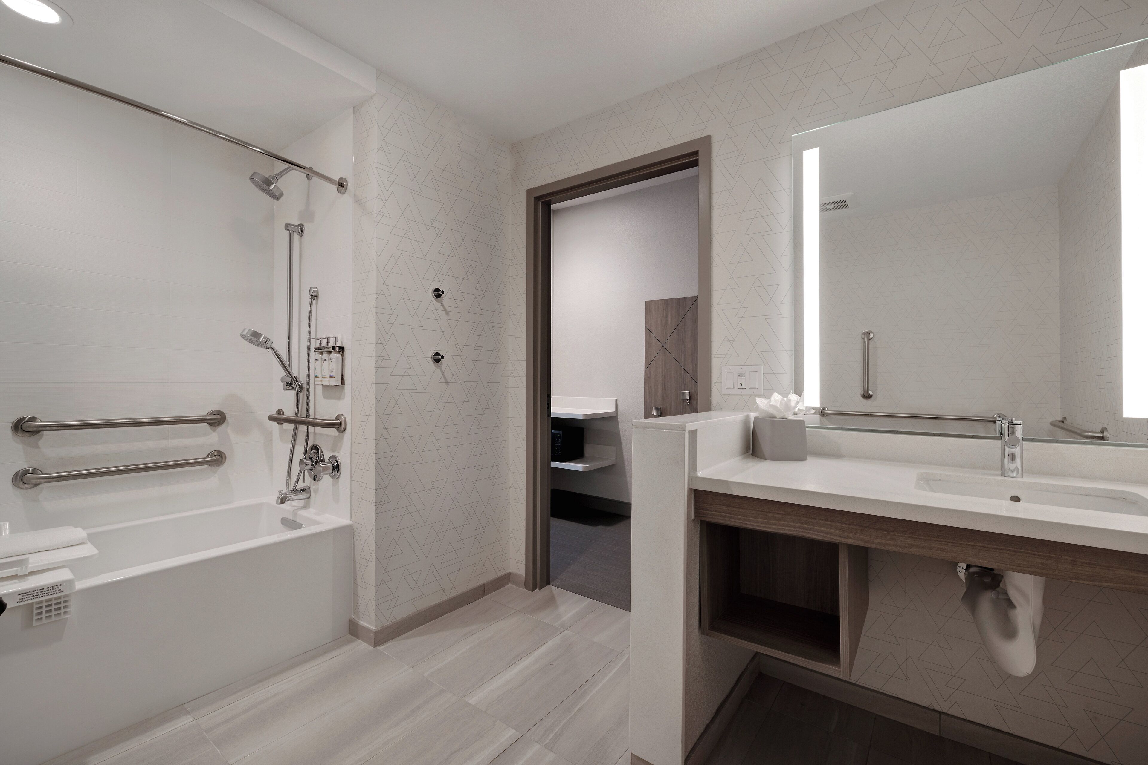 Une salle de bain moderne dotée d’une douche à l’italienne, de barres d’appui, d’un grand miroir et d’un meuble-lavabo avec un évier.