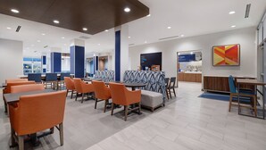A modern dining area with orange chairs and tables, a coffee station, and a view of the city. - Holiday Inn Express & Suites Ontario - Chino Hills by IHG (Chino Hills)