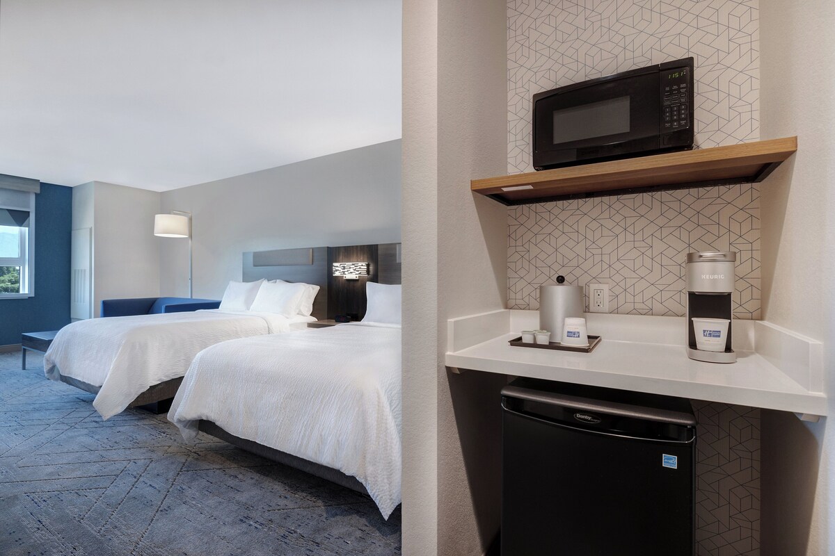 A hotel room with two beds, a microwave, a coffee maker, and a dishwasher.
