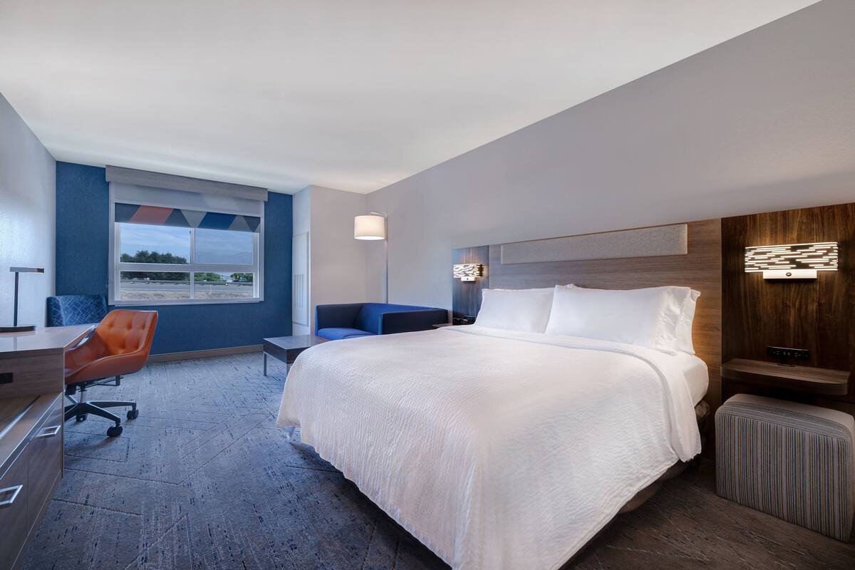 Habitación de hotel moderna con una cama grande, un escritorio, una silla y vistas al exterior a través de una ventana.