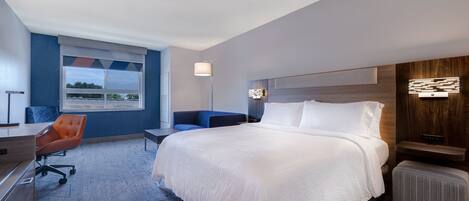 Habitación de hotel moderna con una cama grande, un escritorio, una silla y vistas al exterior a través de una ventana.