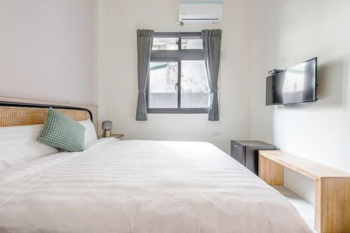 A hotel room with a bed, a bedside table, a TV, and a window with curtains.