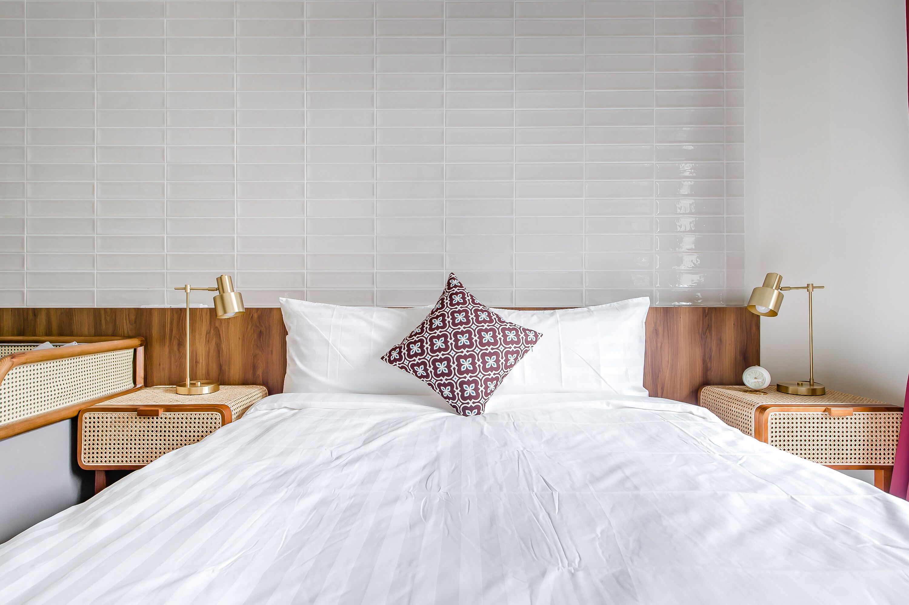 Una cama bien tendida con sábanas blancas, una almohada estampada y dos mesitas de noche con lámparas.