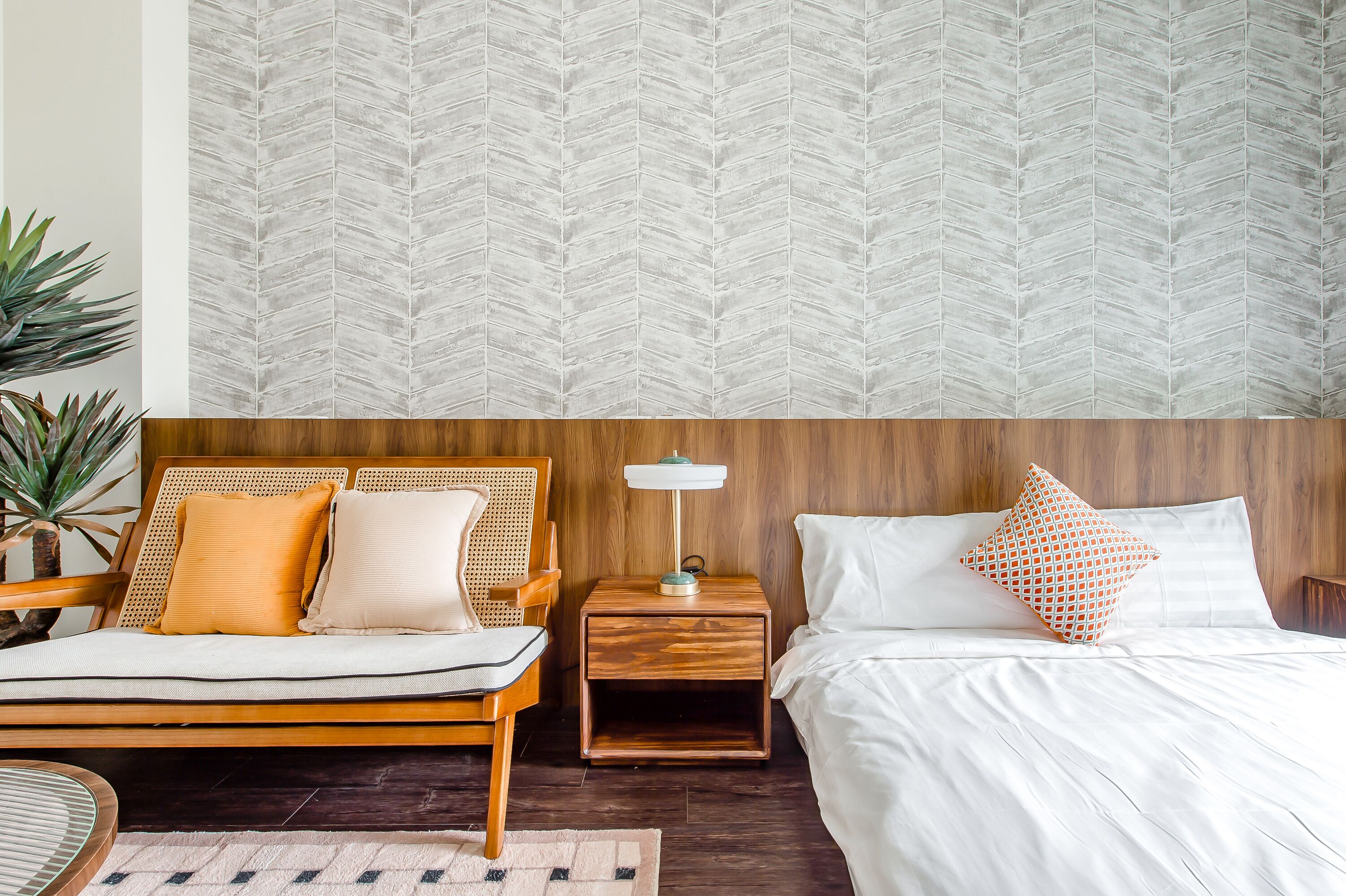 A bedroom with a wooden headboard, a nightstand with a lamp, and a bed with white bedding and patterned pillows.