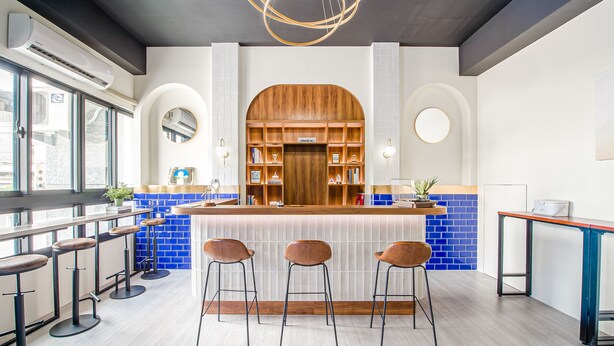 Eine moderne Bar mit Holzbalken, Barhocker und einer blauen Fliesenfassade.