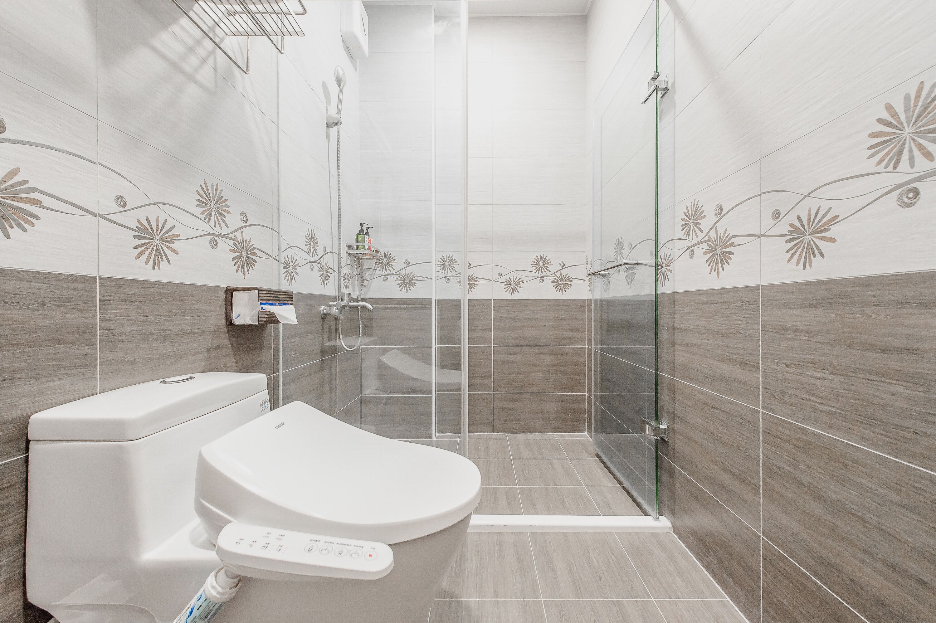 A modern bathroom with a toilet, a glass shower enclosure, and decorative wall tiles.