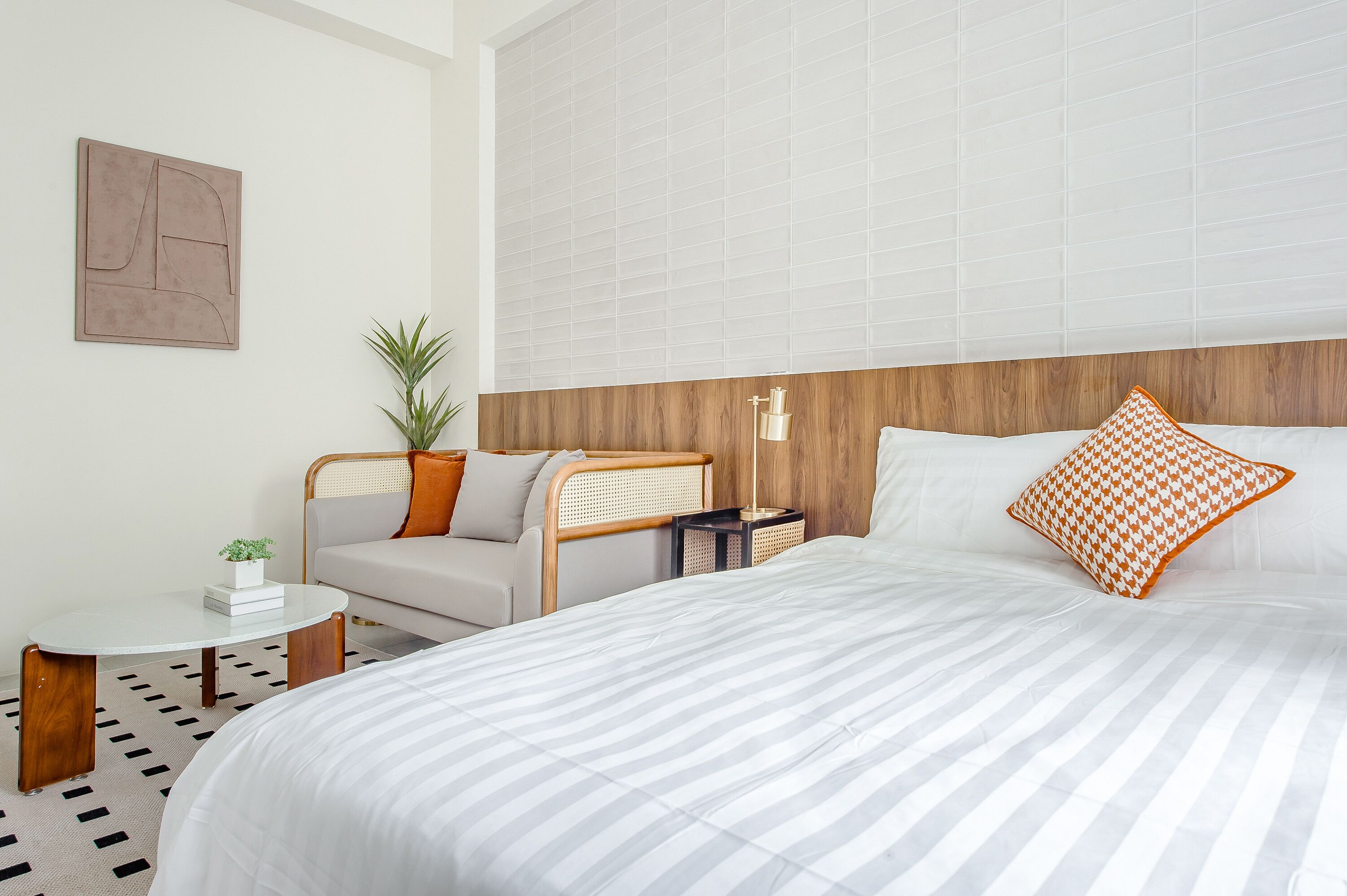 A modern hotel room with a large bed, a small round table, a seating area with a sofa, and a potted plant.