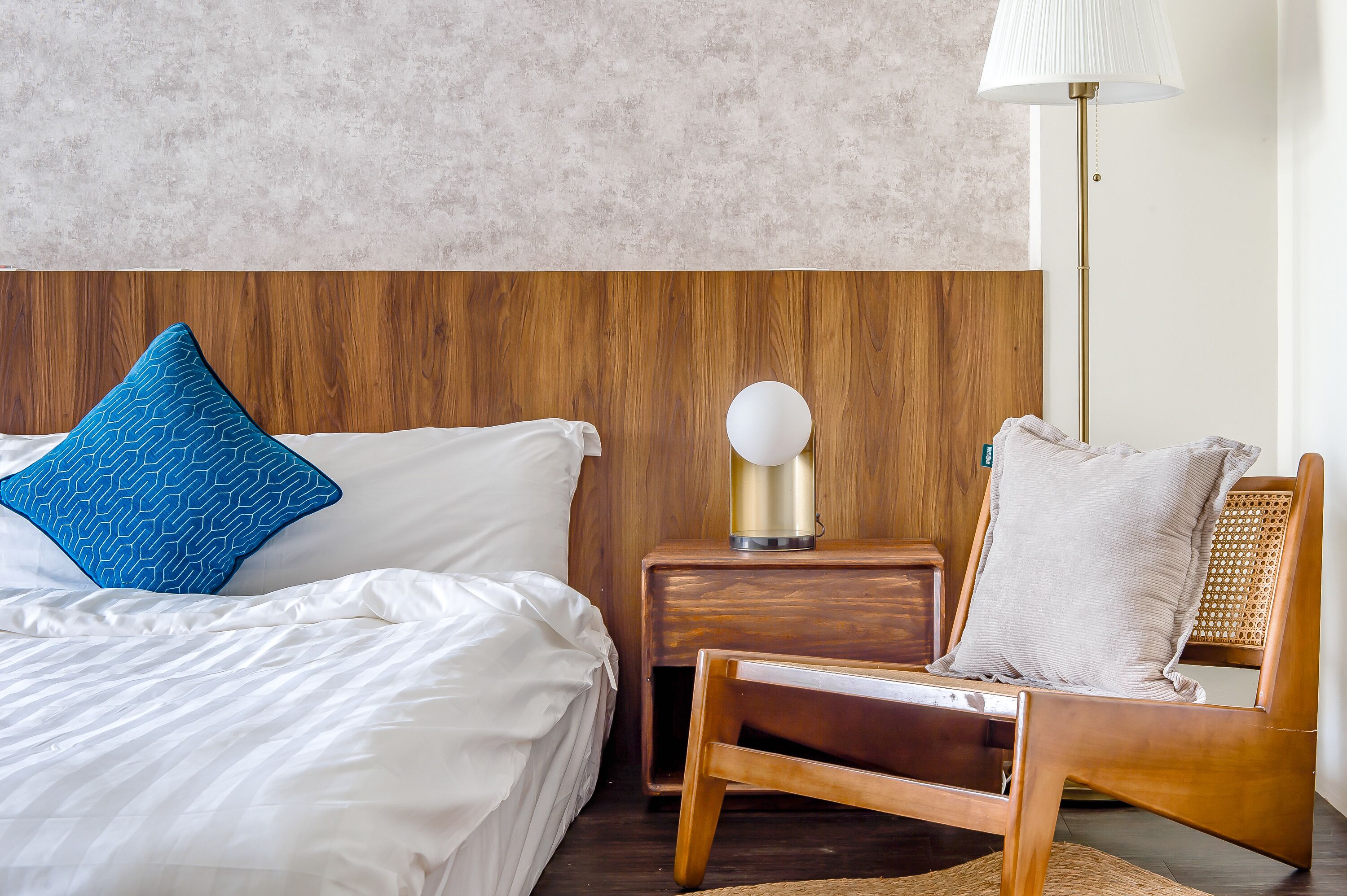 A bedroom with a bed, a nightstand, a lamp, and a wooden chair.