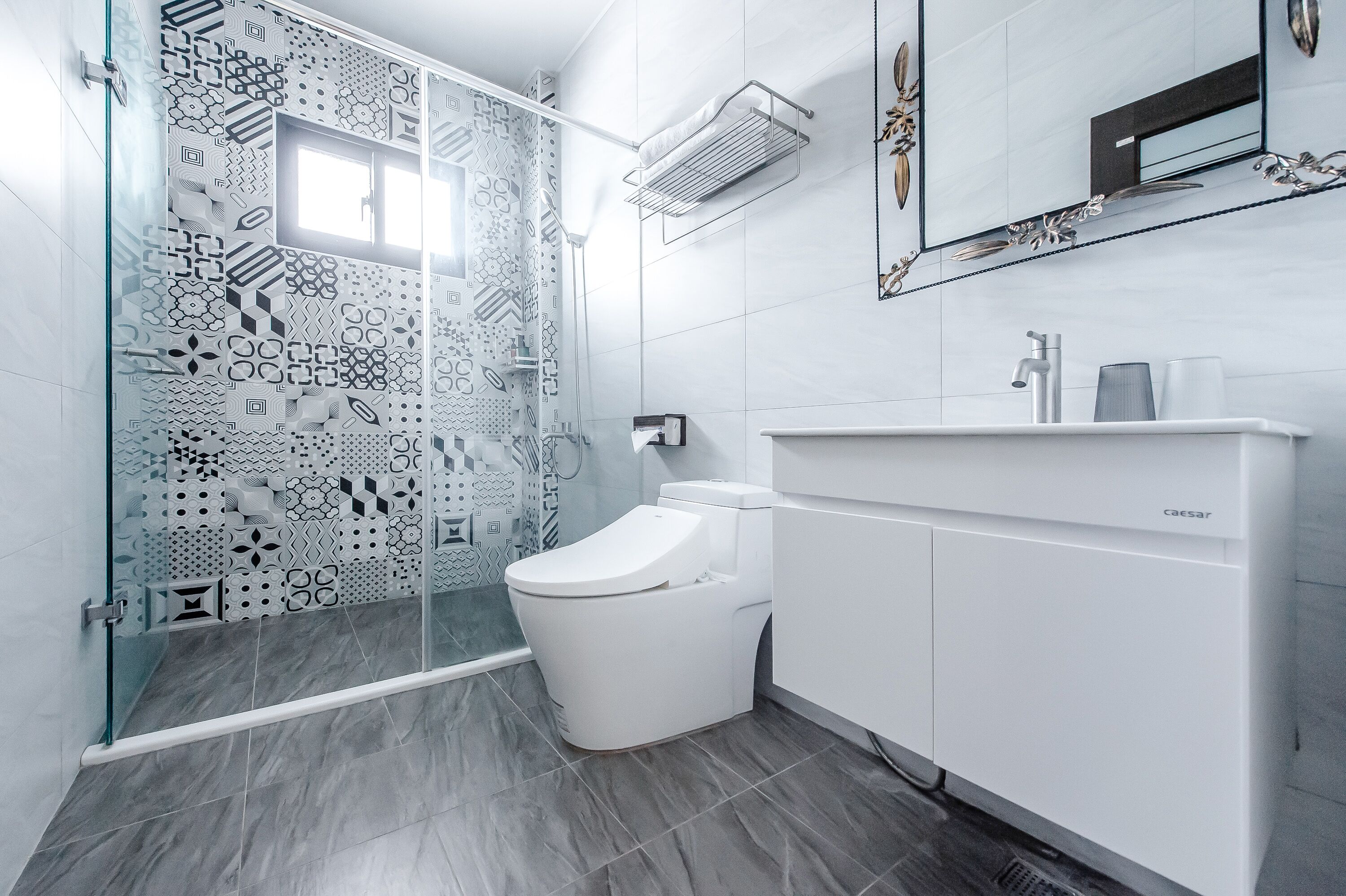 A modern bathroom with a patterned shower wall, a white toilet, and a built-in sink with a cabinet.