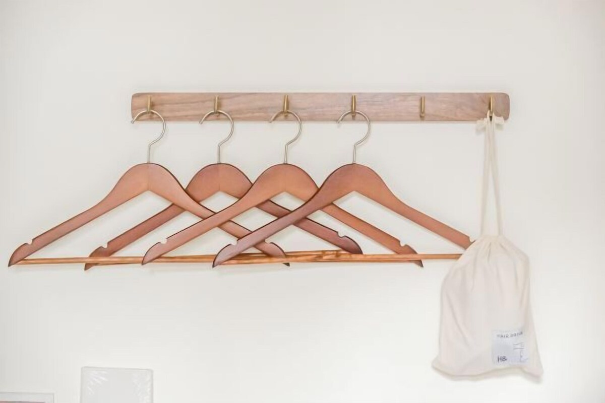A wooden coat rack with five wooden hangers and a white cloth bag.