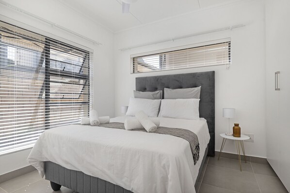 A bedroom with a bed, a bedside table with a lamp, and a window with blinds.