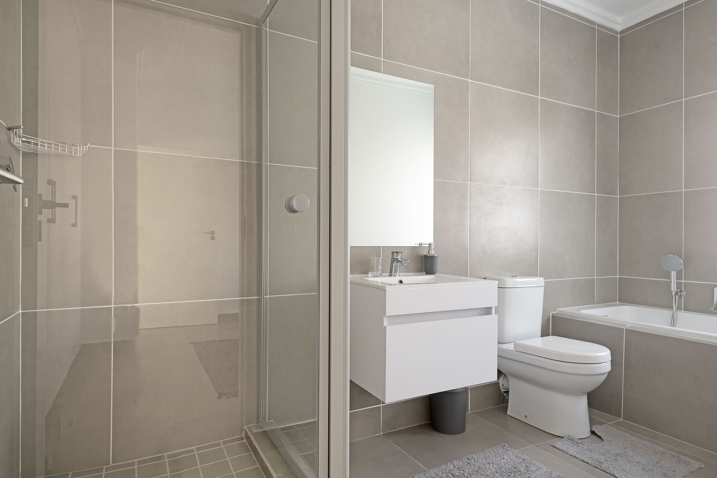Een moderne badkamer met een douchecabine van glas, een witte wastafel, een toilet en een bad.