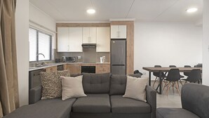 A modern living room with a grey sofa, a dining table with chairs, and a kitchen area with cabinets and appliances. - Ballito Village 69 by HostAgents (Ballito)