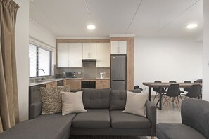 A modern living area with a grey sofa, a dining table with chairs, and a kitchen with white cabinets and a refrigerator.