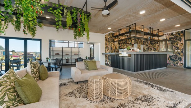A modern interior with a sofa, two round wicker ottomans, a ceiling fan, and hanging plants. - Ballito Village 69 by HostAgents (Ballito)