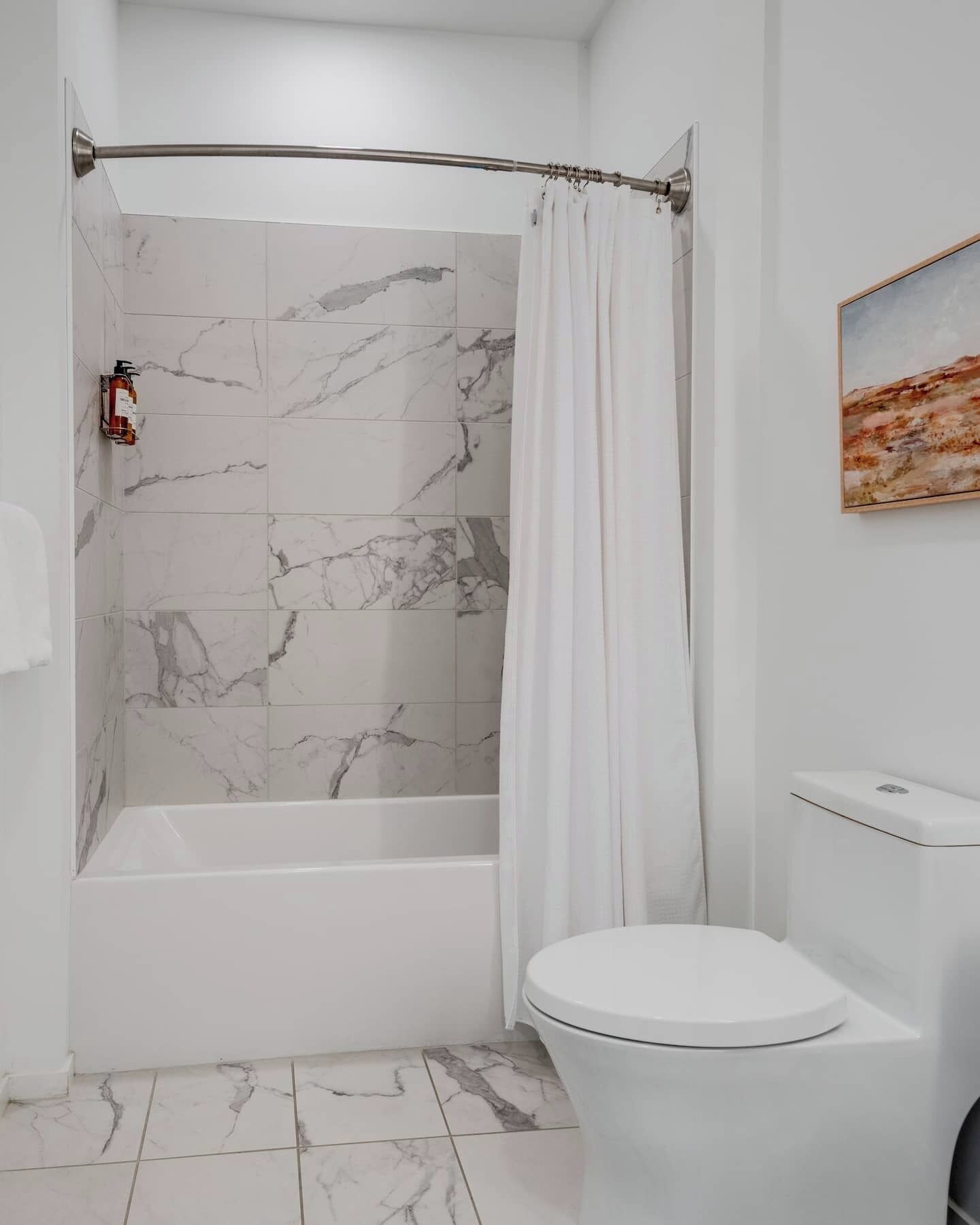 A bathroom with a shower, toilet, and marble tiles.