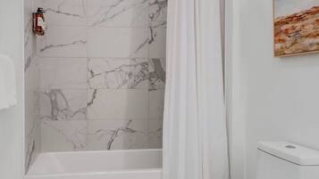A bathroom with a shower, toilet, and marble tiles.