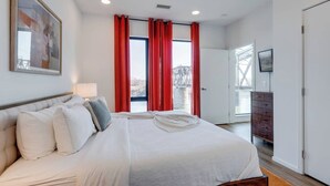 Een moderne hotelkamer met een groot bed, rode gordijnen, een televisie en uitzicht op een brug.