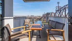 Een balkon met een tafel en stoelen, met uitzicht op een rivier en een brug.