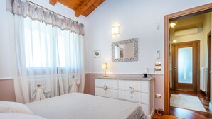 A bedroom with a bed, a dresser, a mirror, and a door leading to another room. - GuestHost - Cozy Apt with Terrace and Private parking! x4 (Gonars)