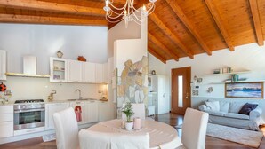 A modern kitchen with white cabinets, a stone accent wall, and a dining area with a round table and chairs. - GuestHost - Cozy Apt with Terrace and Private parking! x4 (Gonars)