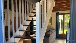 Una escalera de madera con barandillas blancas que lleva a un espacio de estar con un sofá y vistas al exterior.