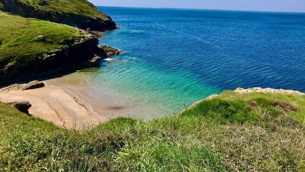 Un paisaje costero con una vista despejada del mar, colinas cubiertas de hierba y una playa de arena.