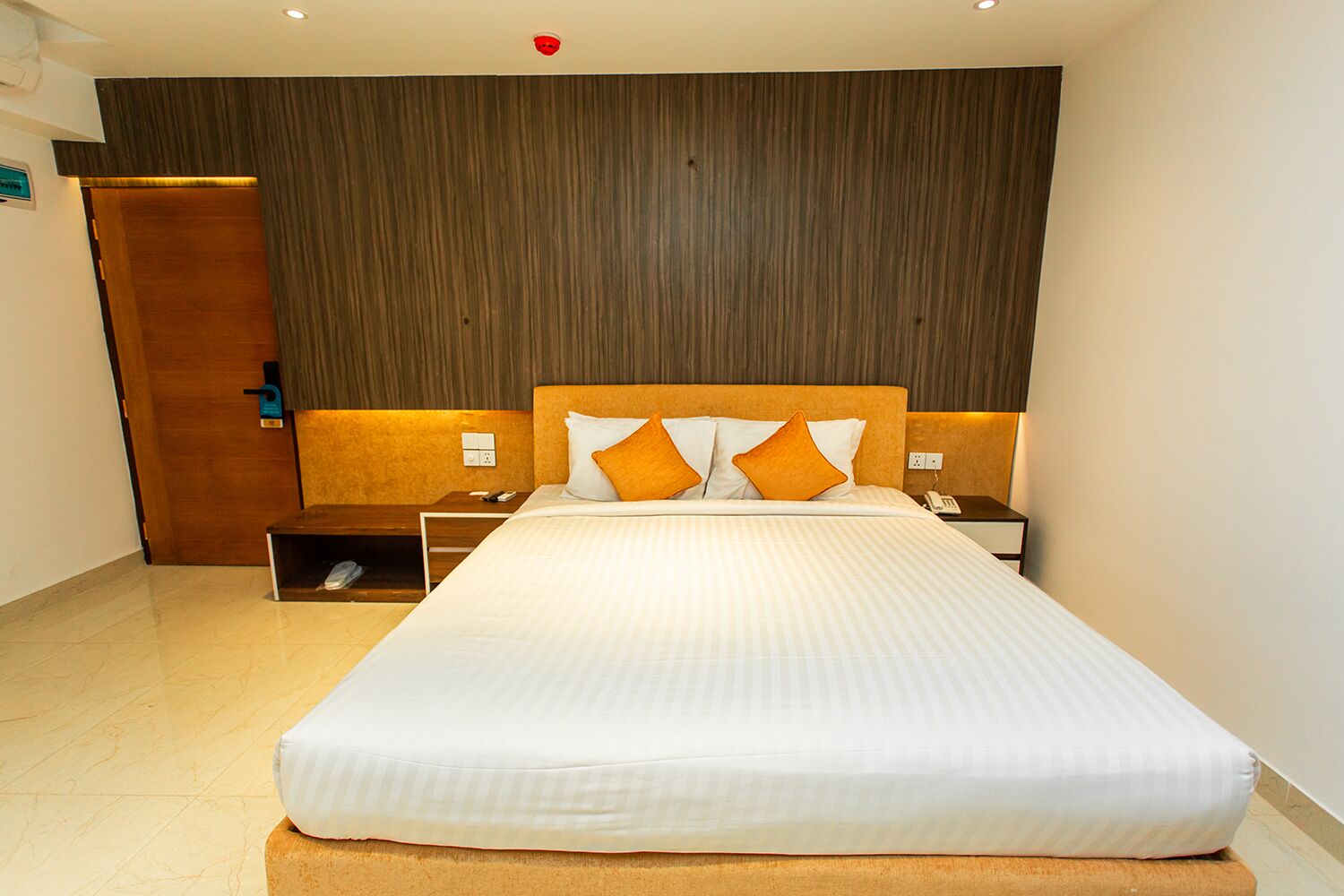 Una habitación de hotel con una cama grande, cabecera de madera, dos mesitas de noche y un armario de madera.