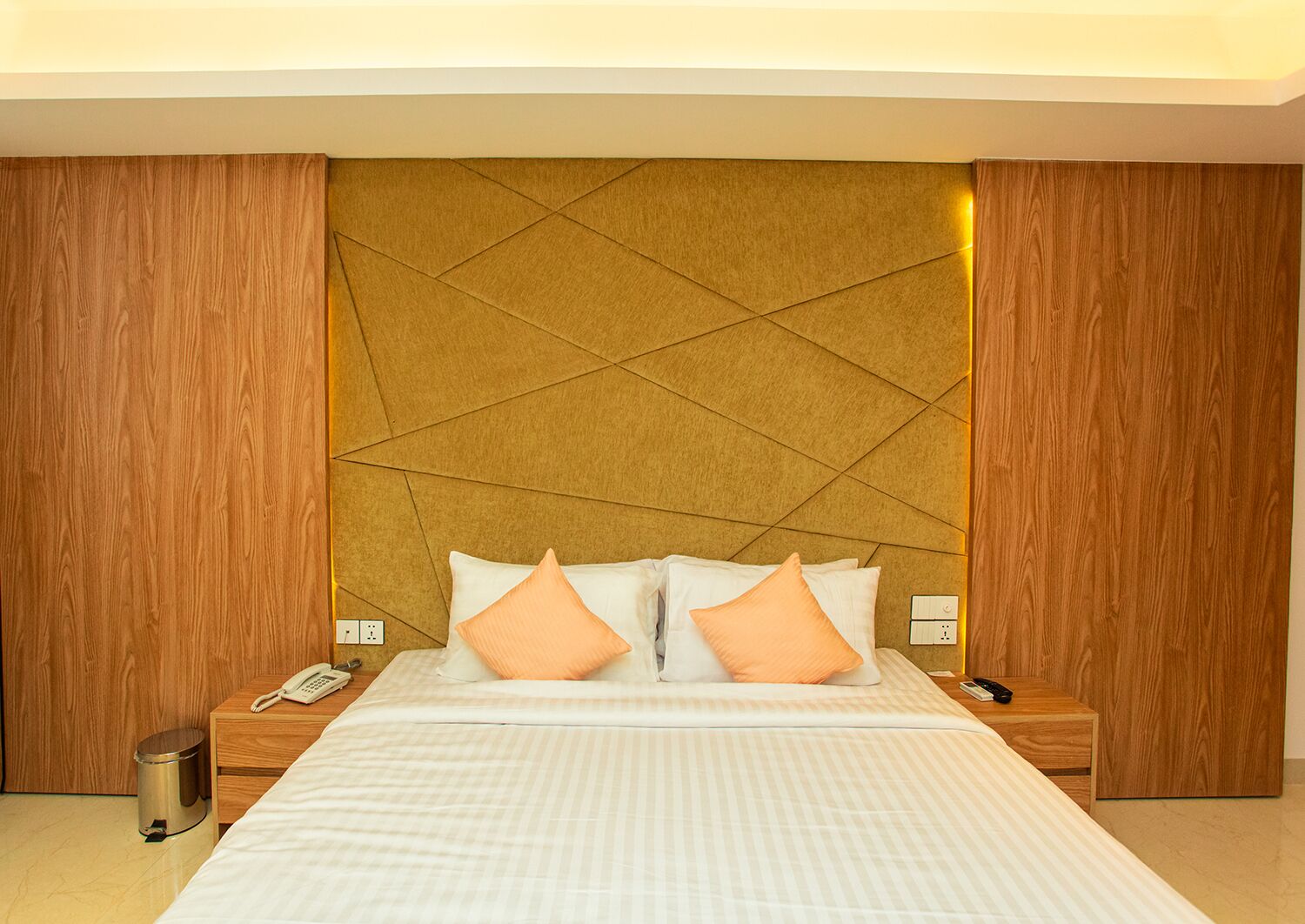 Een hotelkamer met een groot bed, twee nachtkastjes, een telefoon en een prullenbak.