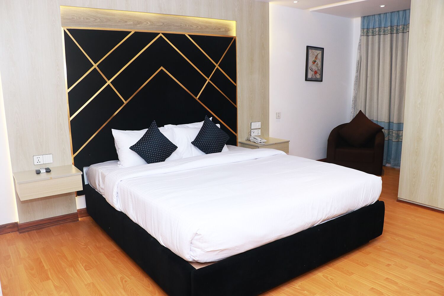 Een moderne hotelkamer met een groot bed, een houten hoofdbord, een nachtkastje met telefoon en een stoel.