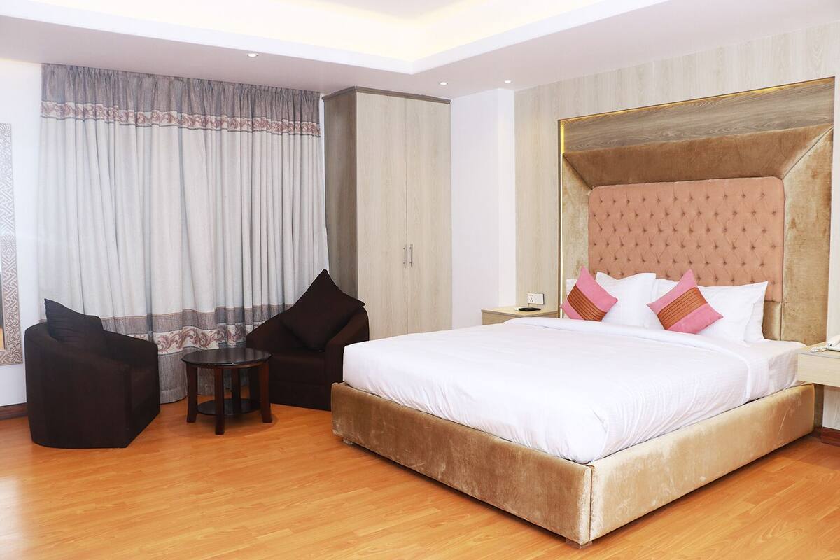 A hotel room with a large bed, two armchairs, a small table, and a nightstand with a phone.