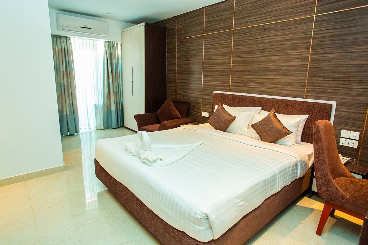 A modern hotel room with a large bed, brown headboard, and a wooden accent wall.