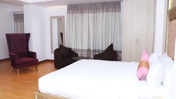 Habitación de hotel con una cama grande, dos sillones, un espejo y un armario.