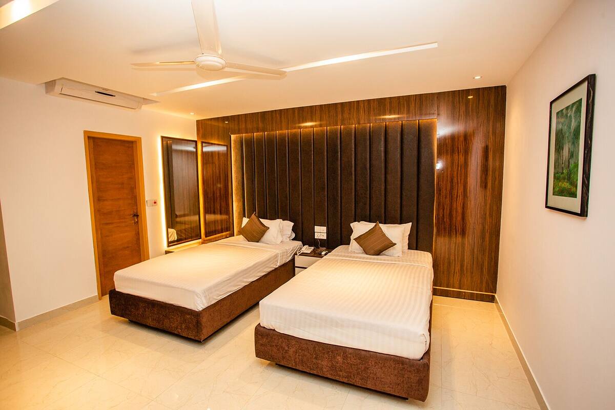 A modern hotel room with two beds, a ceiling fan, and a large mirror.