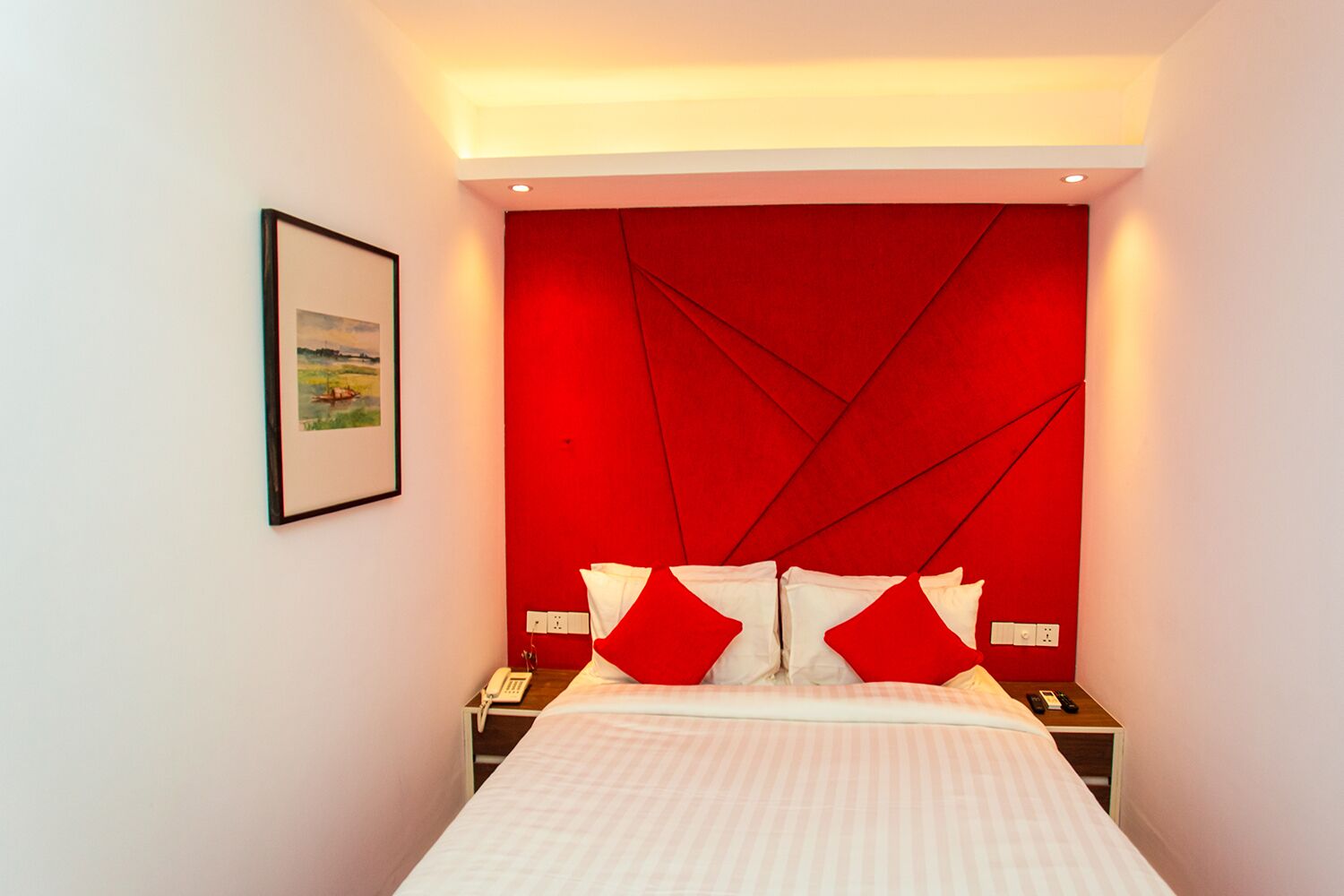 Quarto de hotel com cama, mesa de cabeceira, quadro na parede e parede decorada em vermelho.