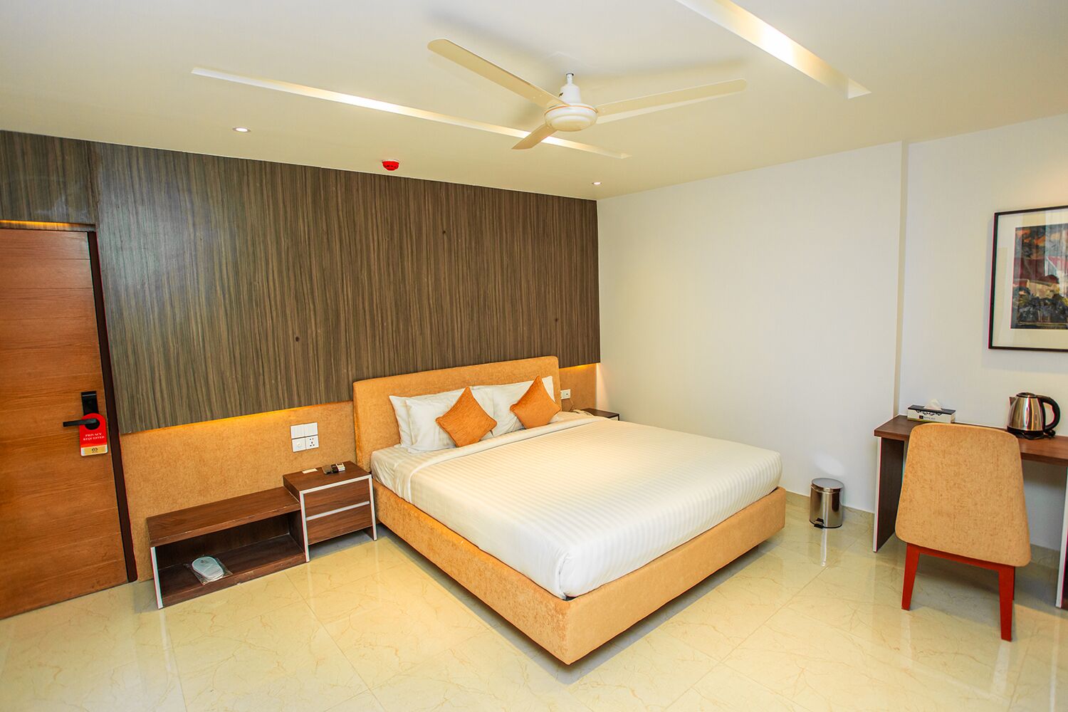 A hotel room with a bed, bedside table, chair, desk, and a ceiling fan.