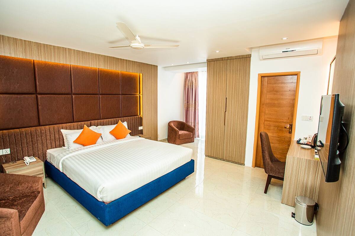 A hotel room with a large bed, a desk, a chair, a television, and a wardrobe.