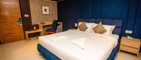 A hotel room with a large bed, a desk, a chair, and a small table.